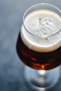 High angle view of a glass filled with frothy beer, showcasing the foam head and rich amber color.